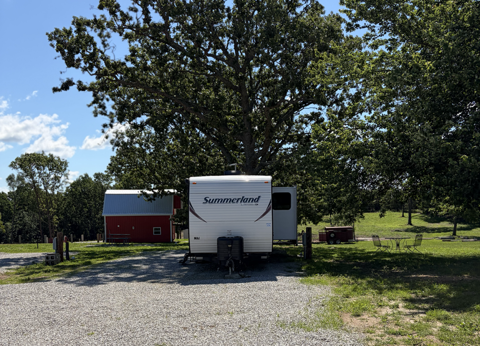 Full hookup RV site at 4 Seasons RV Park in Mansfield, Missouri with a spacious gravel site, mature shade trees, and picnic table.